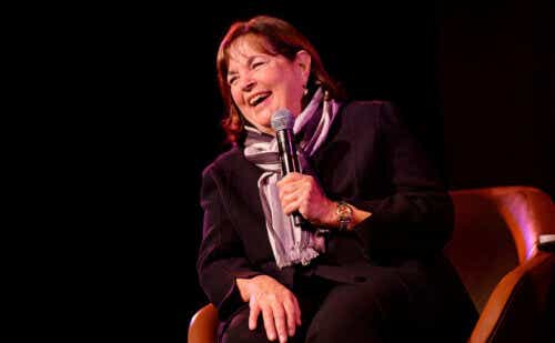 A seated Ina Garten laughs into a microphone on a dimly lit stage.