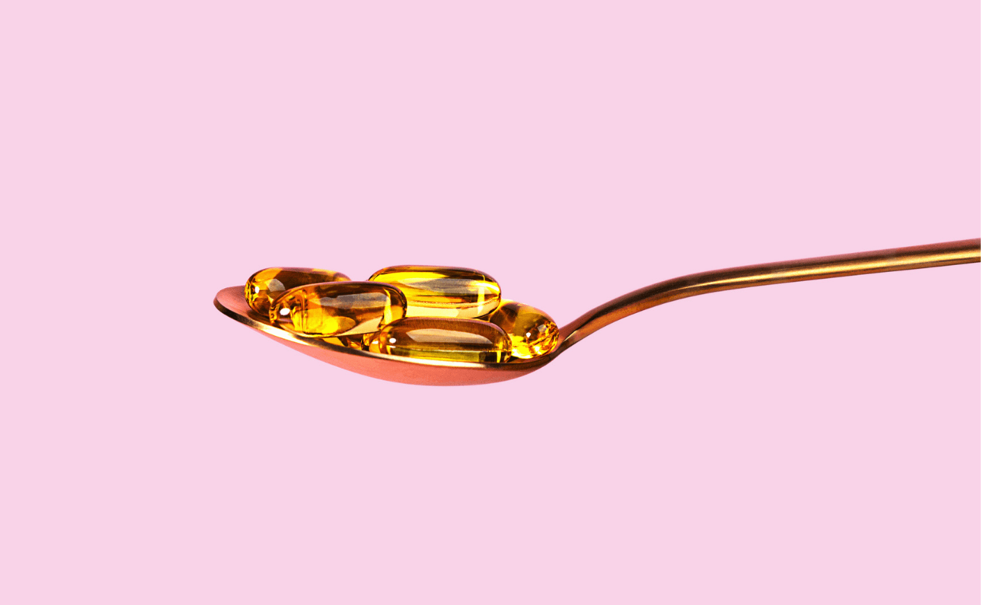 picture of a spoon with vitamin D capsules against pink background
