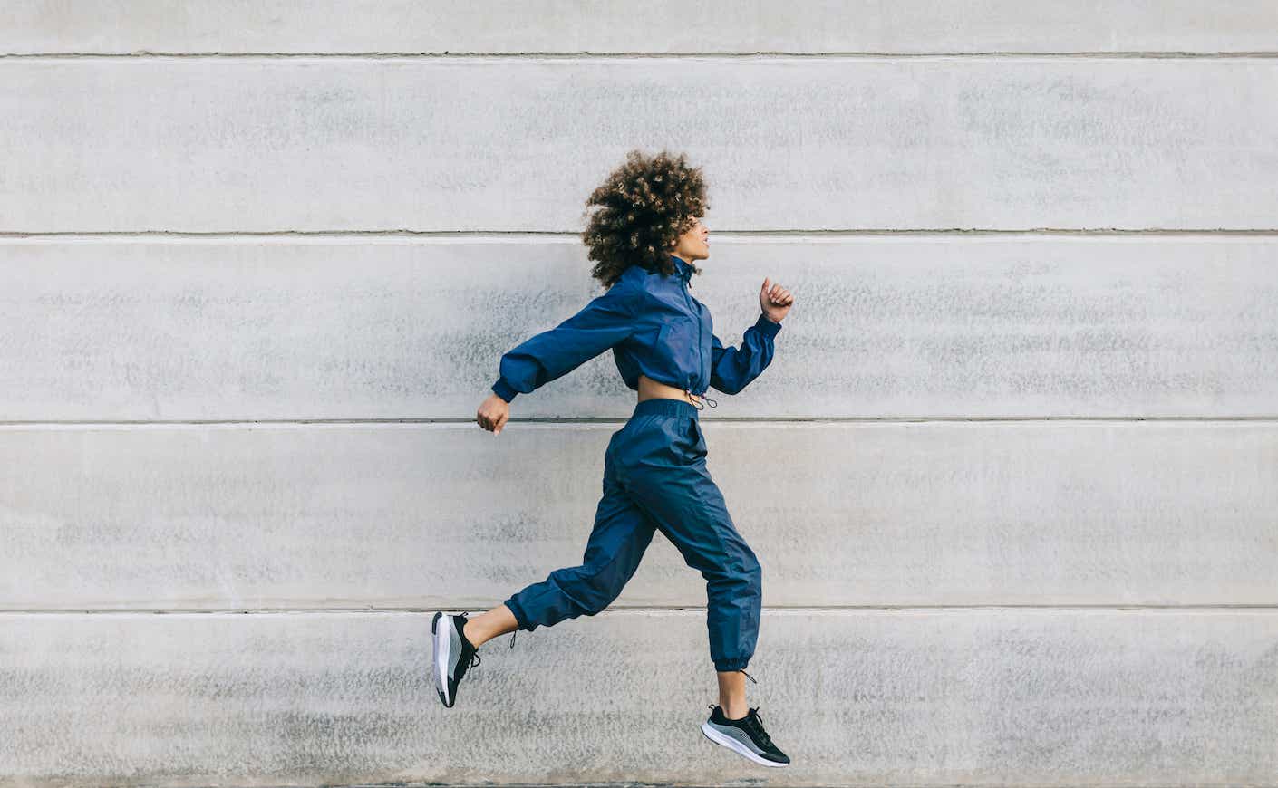 Stylish young woman running along concrete wall