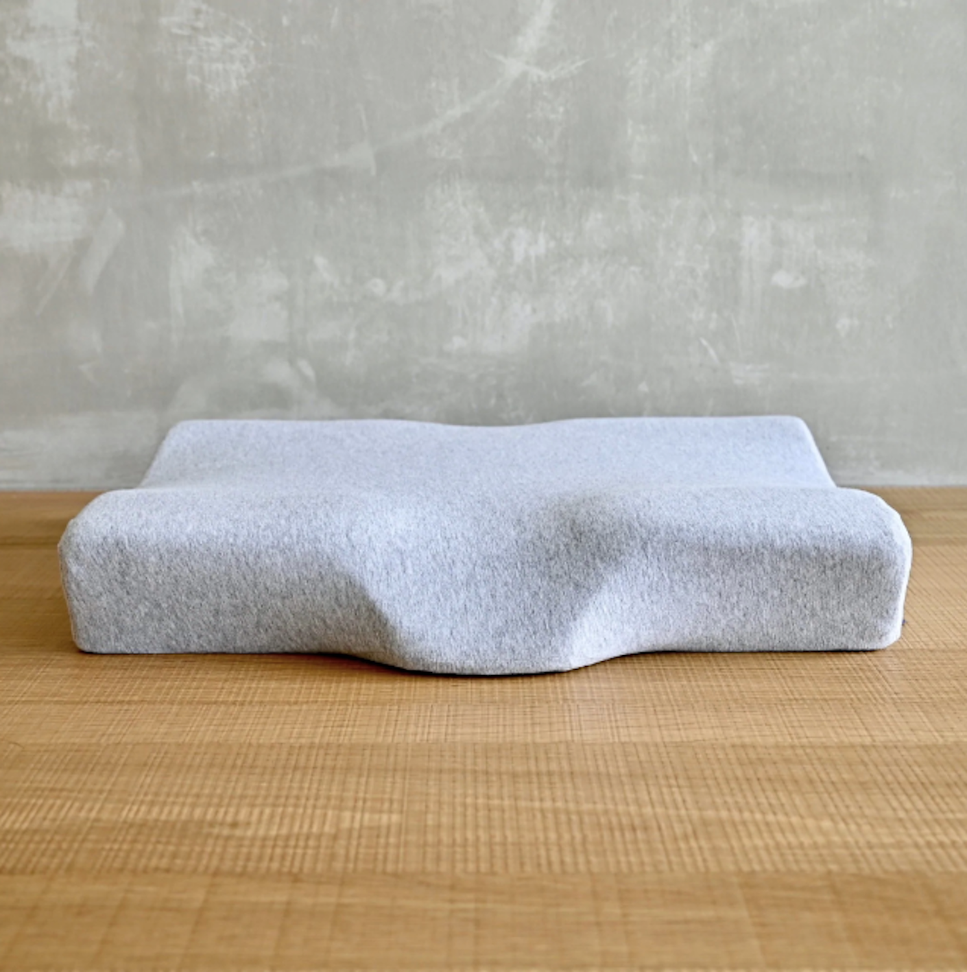 A gray, foam, neck cushion lies flat on a wooden sruface.