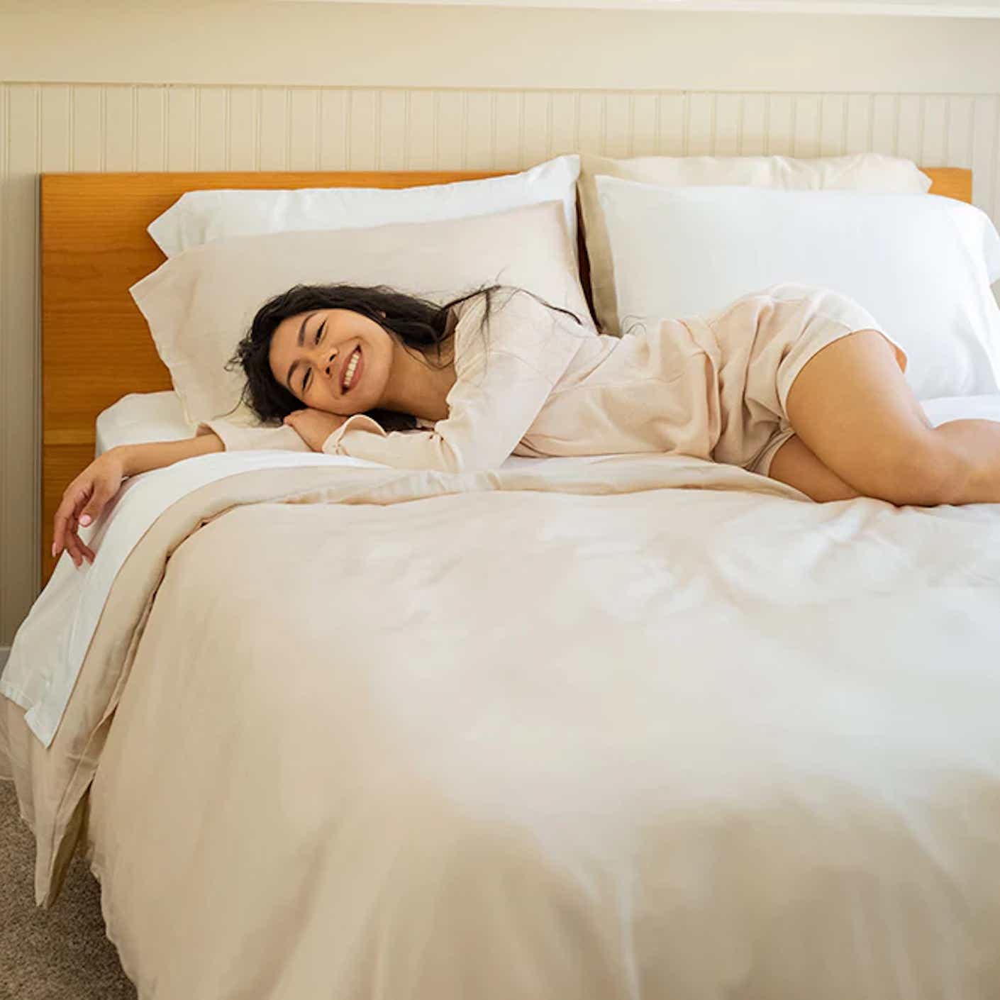 A woman lounges happily on soft yet crips sheets.