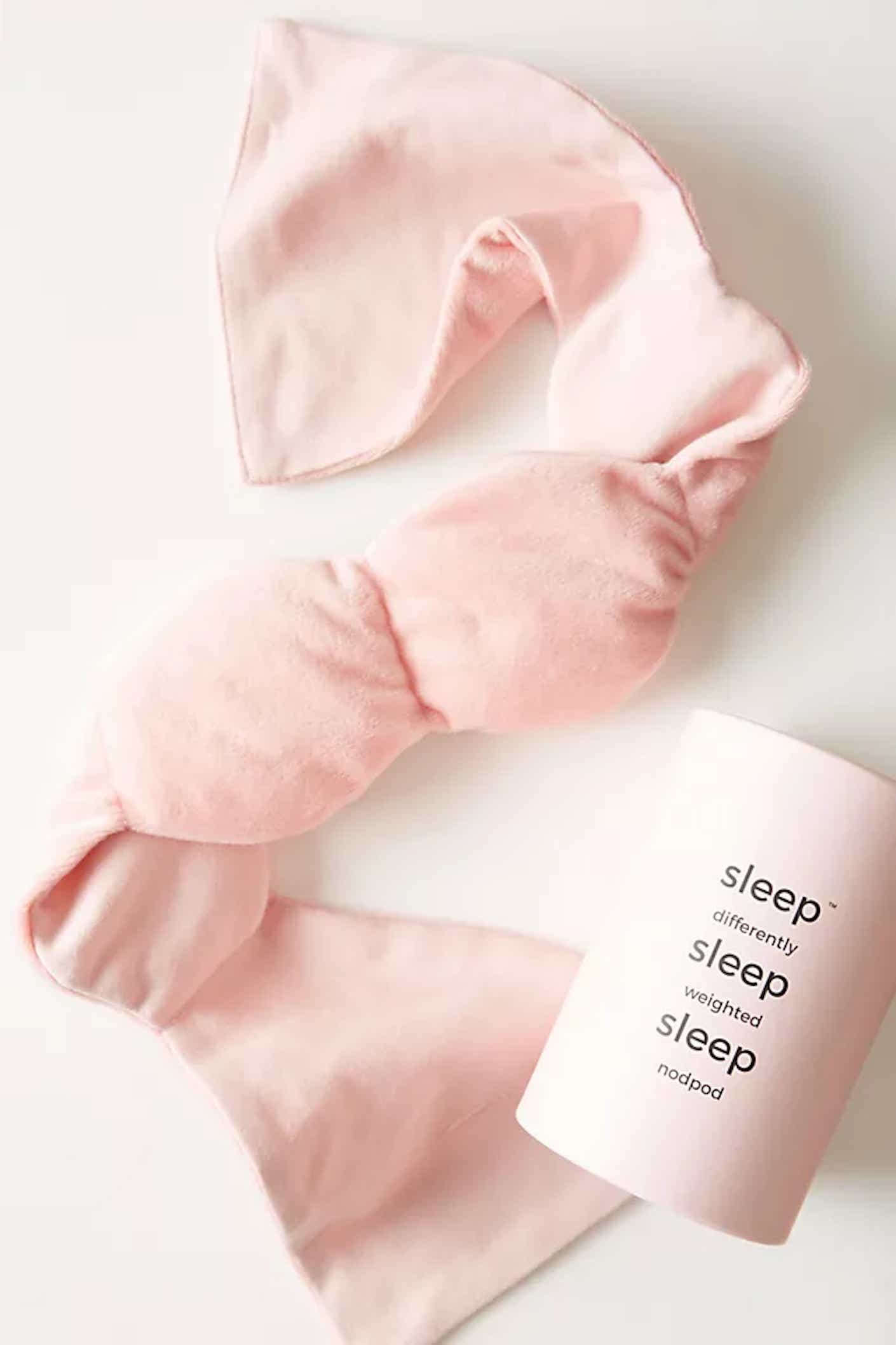 A soft, fuzzy, pink, weighted eye mask lies flat.