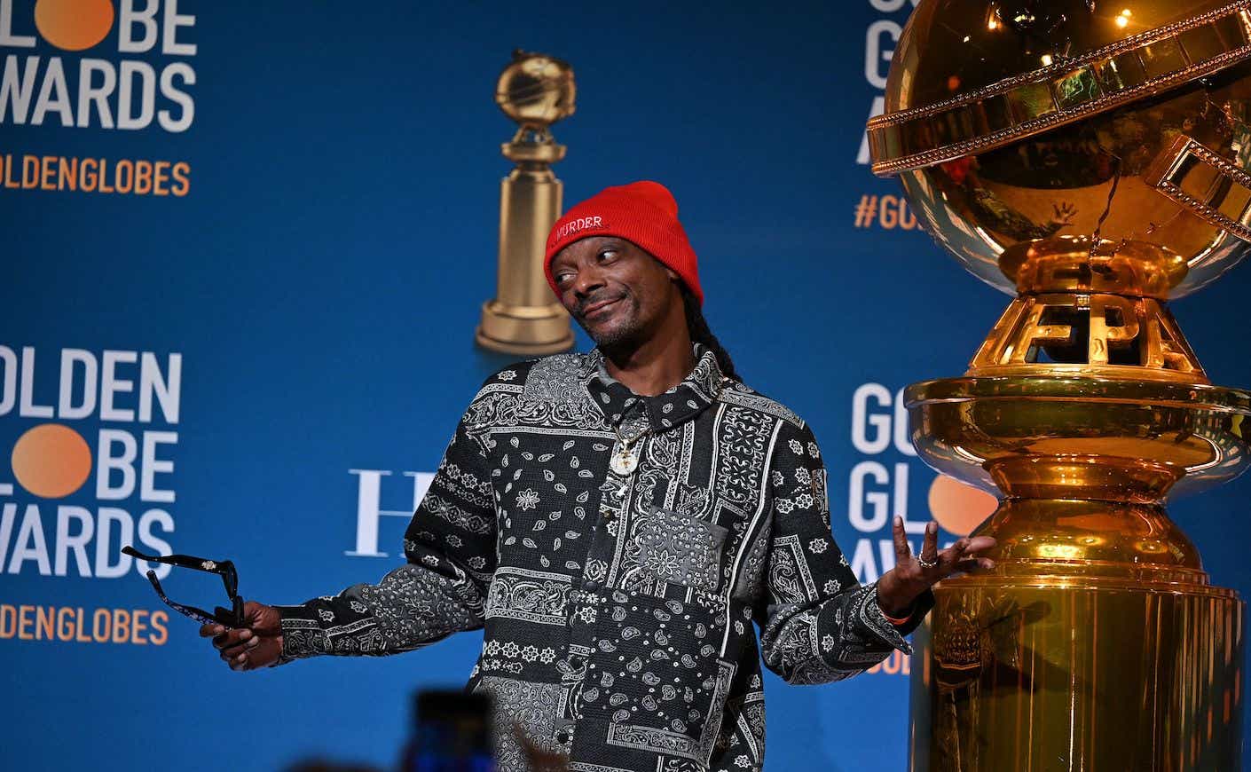 snoop dogg shrugging on stage next to golden globe statue