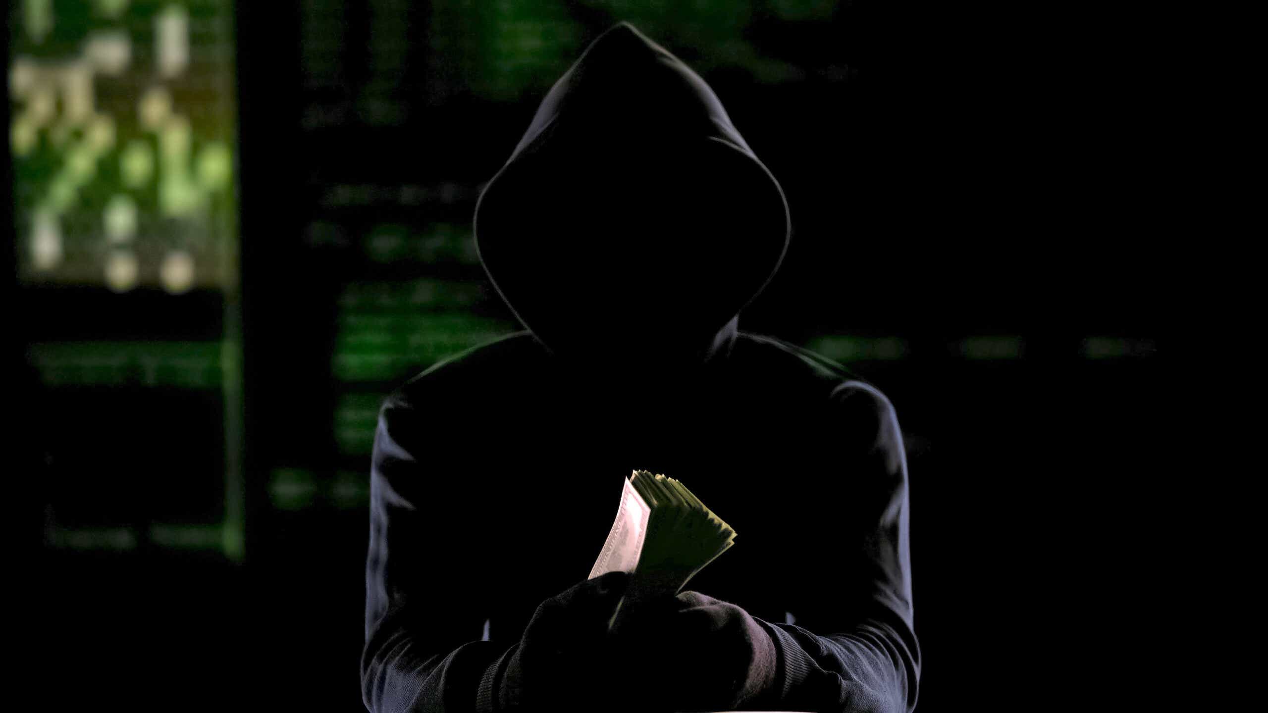 Hooded man in darkness holding cash, murder-for-hire reward or stolen money