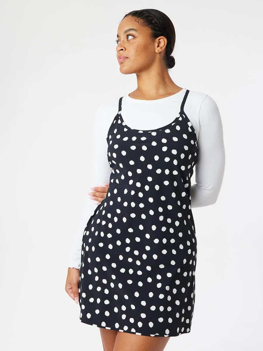 model displaying black printed dress with white dots over a long sleeves white shirt