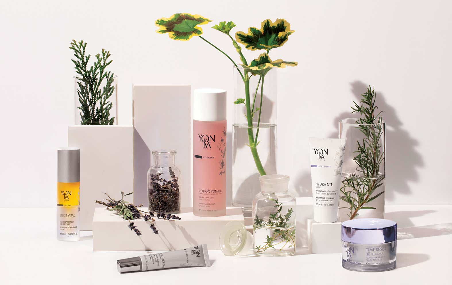 Yon-Ka products and flowers on a white table with a white wall behind