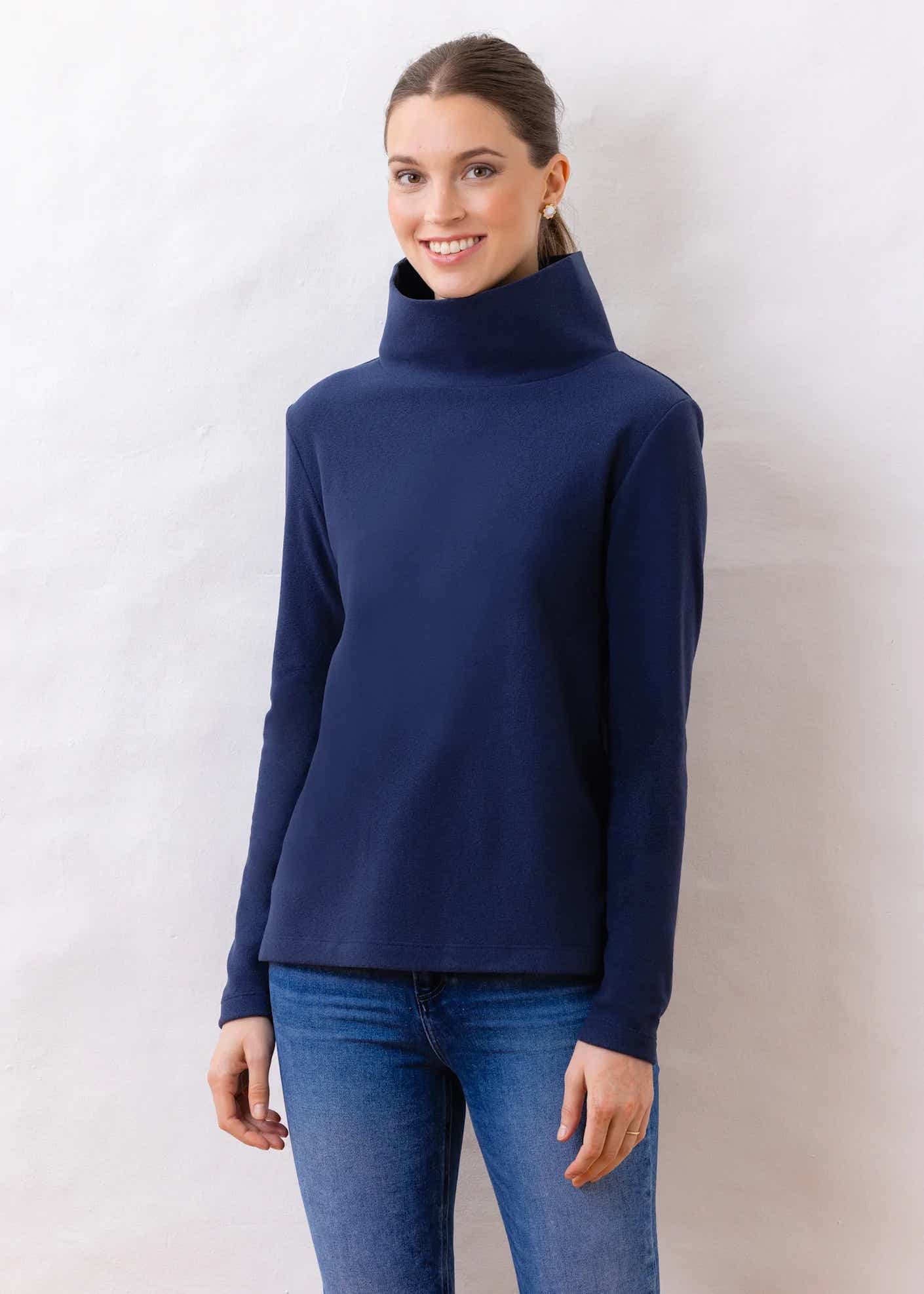 A woman stands posing in a turtleneck.