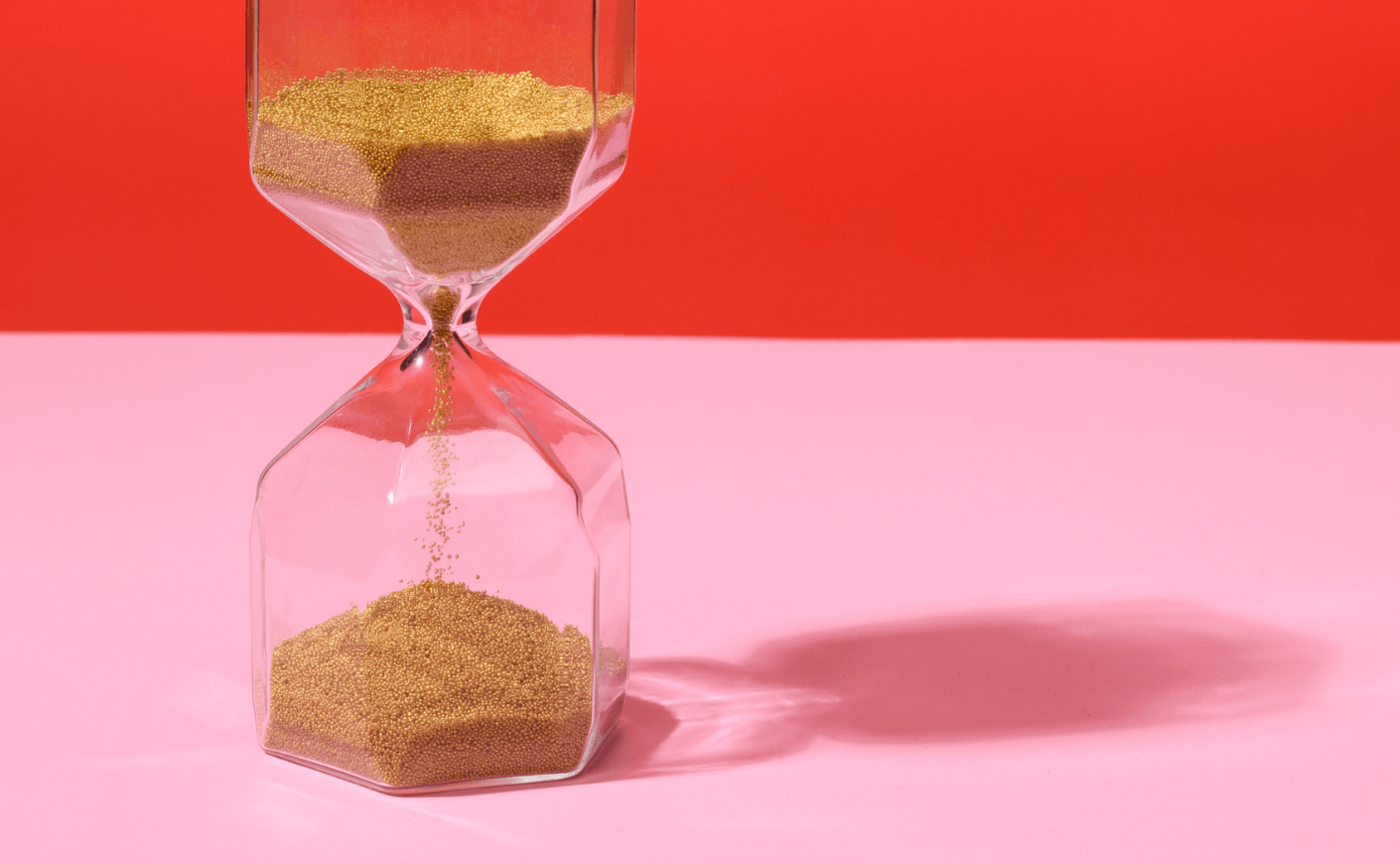 an hourglass with sand on a pink and red background