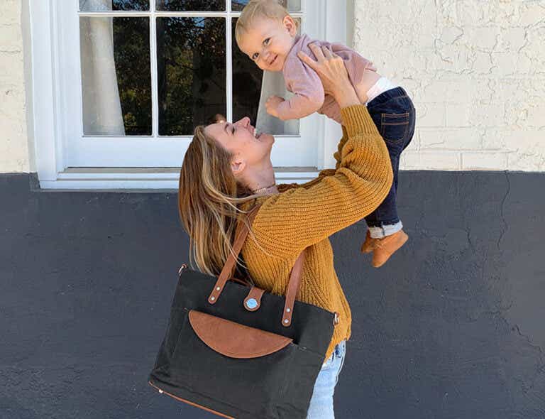 Woman carrying Momkindness tote and playing with a baby