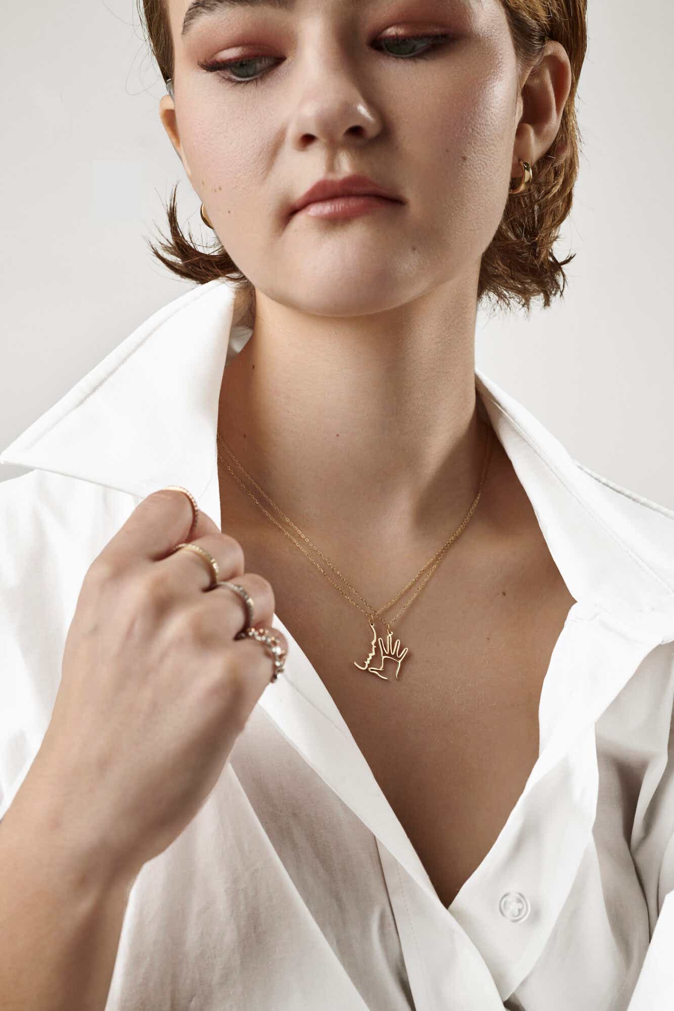 actress millicent simmonds showing the necklace she designed that features the sign for "mom" in ASL