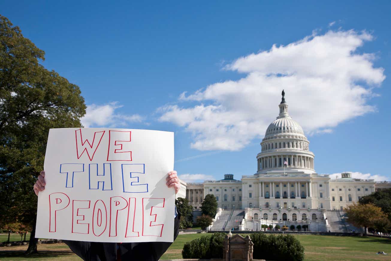 A protestor holding a placard saying "We the People" in front of the US Capitol Building