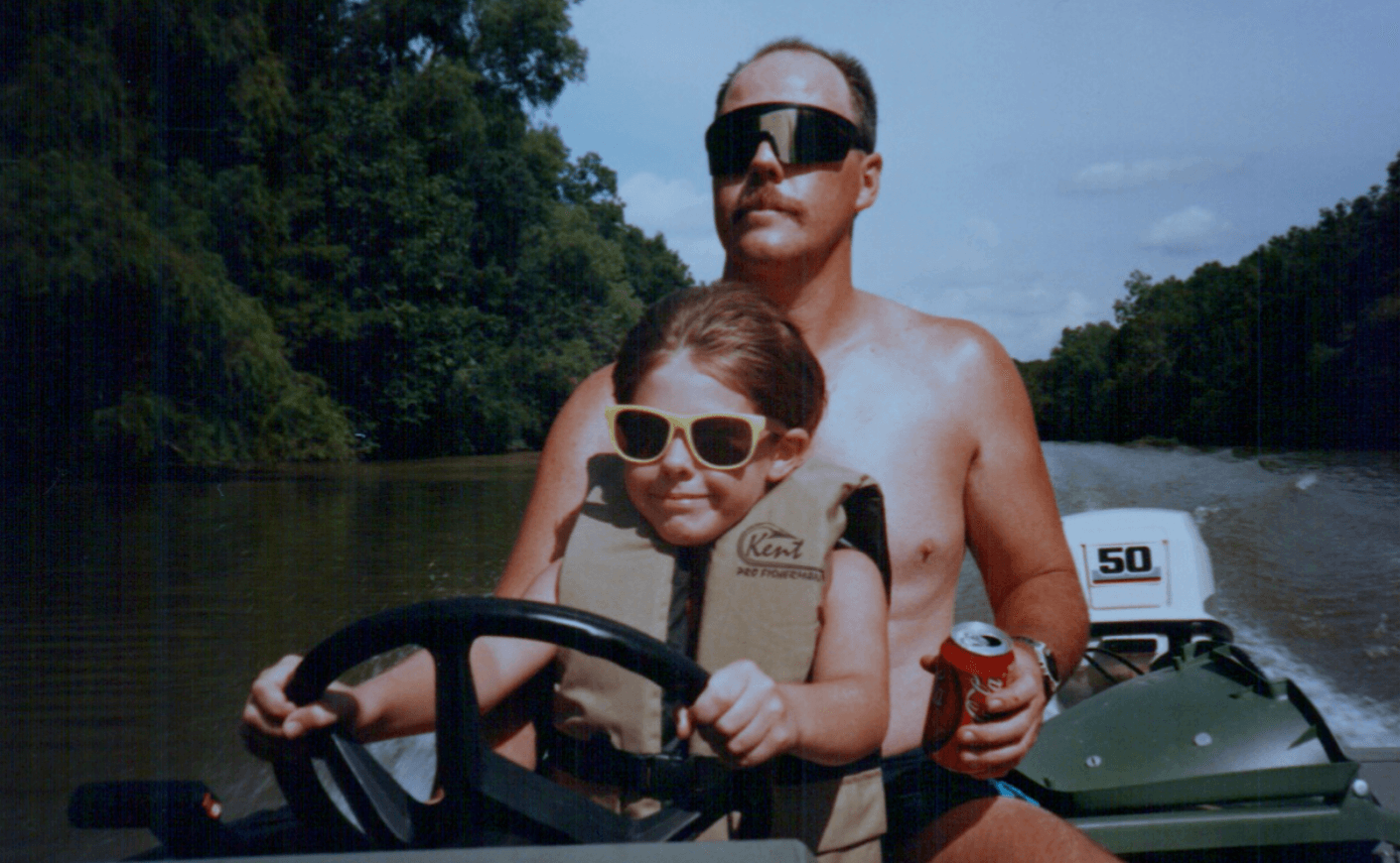 a boy and his father drive a boat on a lake