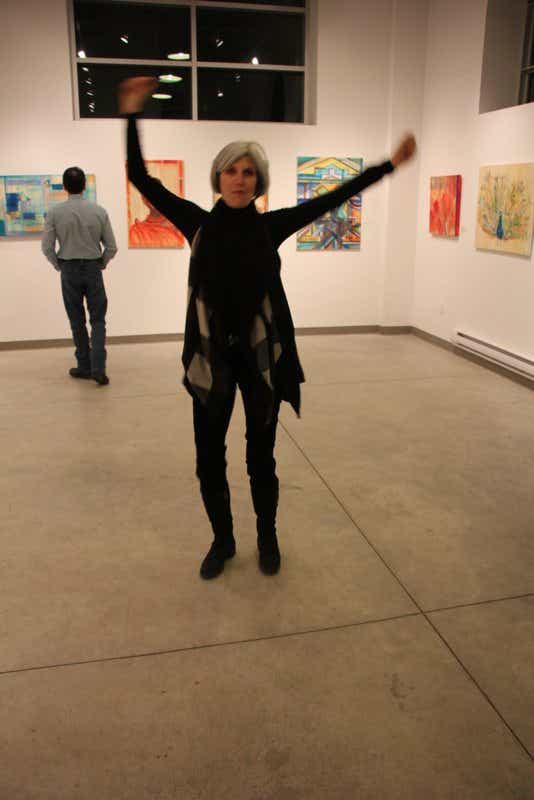 Janice raises her hands at a gallery in front of paintings