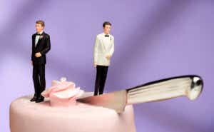 A wedding cake with two groom cake toppers and a knife between them