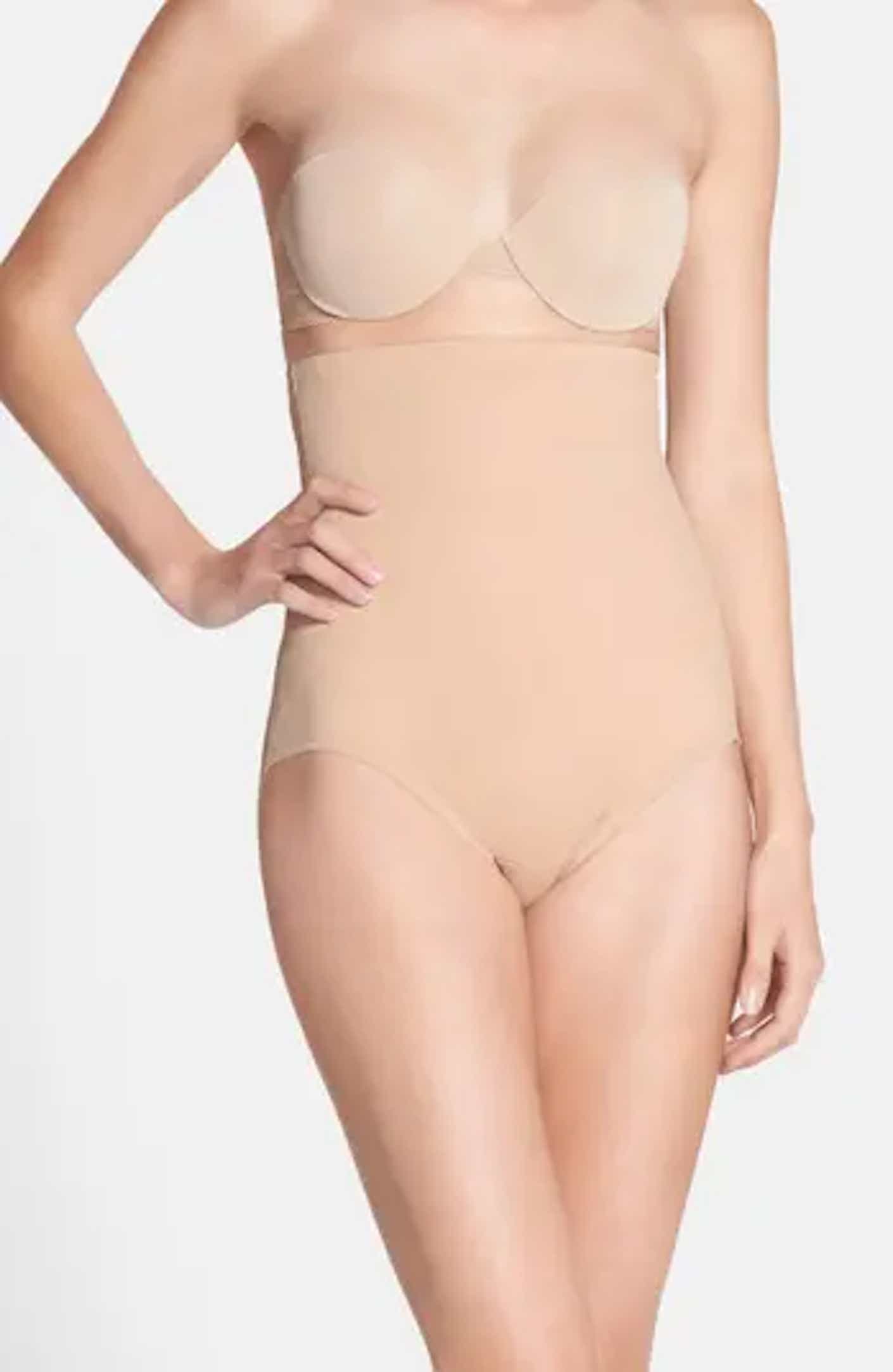 A person poses in a high-waisted, beige shapewear brief and strapless beige bra.