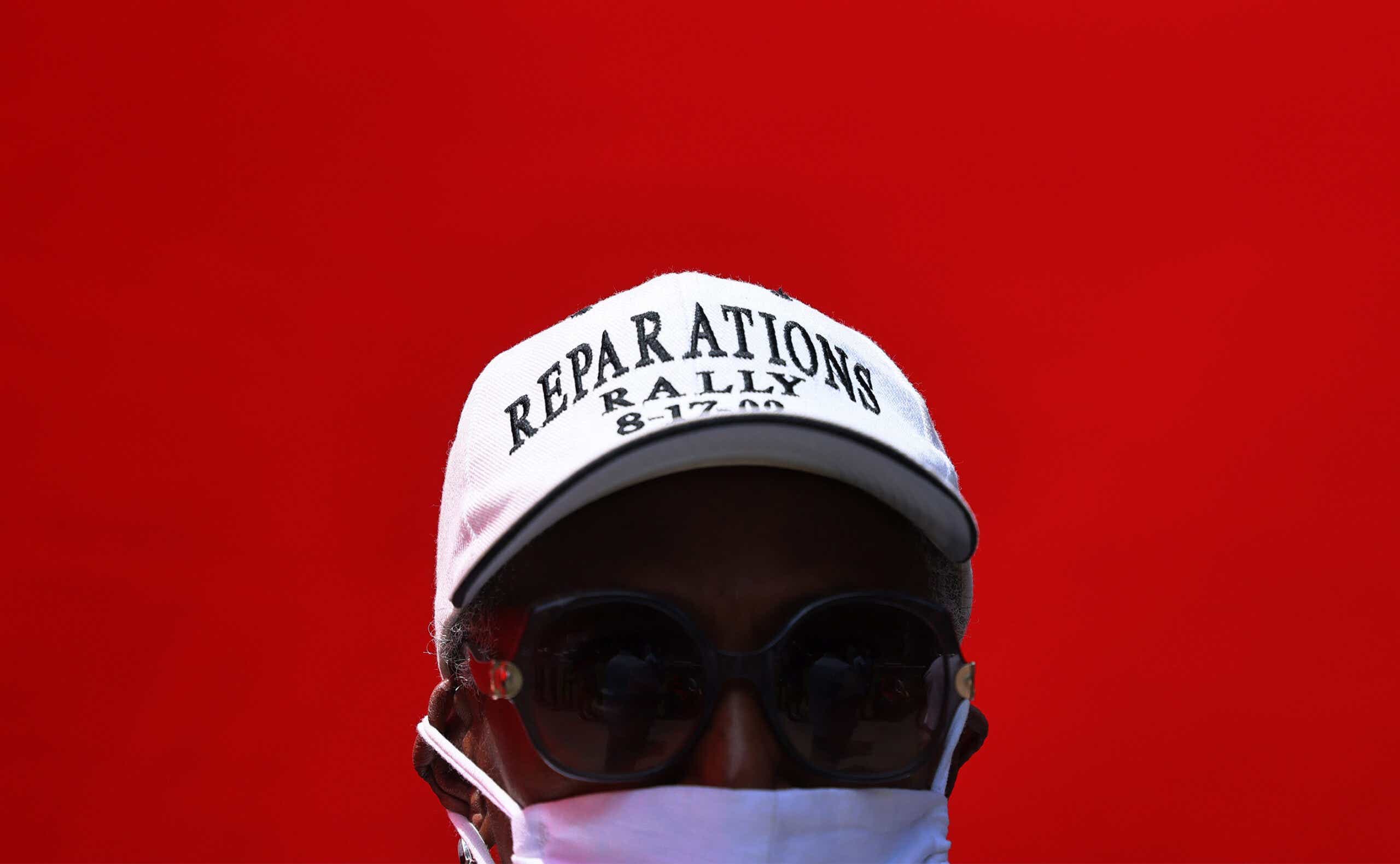 a man wears a hat that reads "reparations rally"