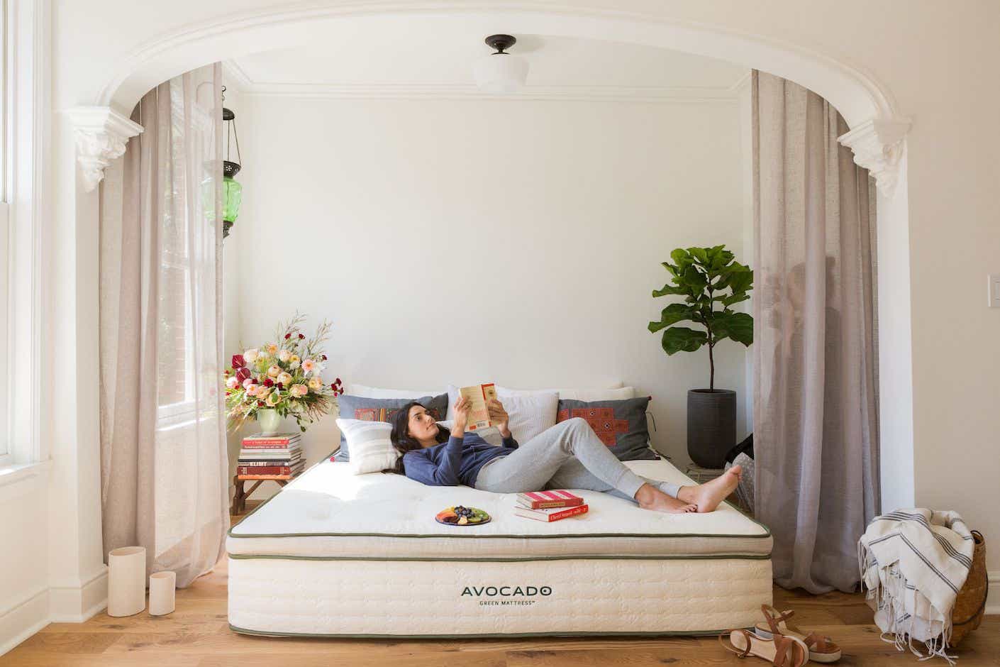 a woman laying on an Avocado brand mattress in a room