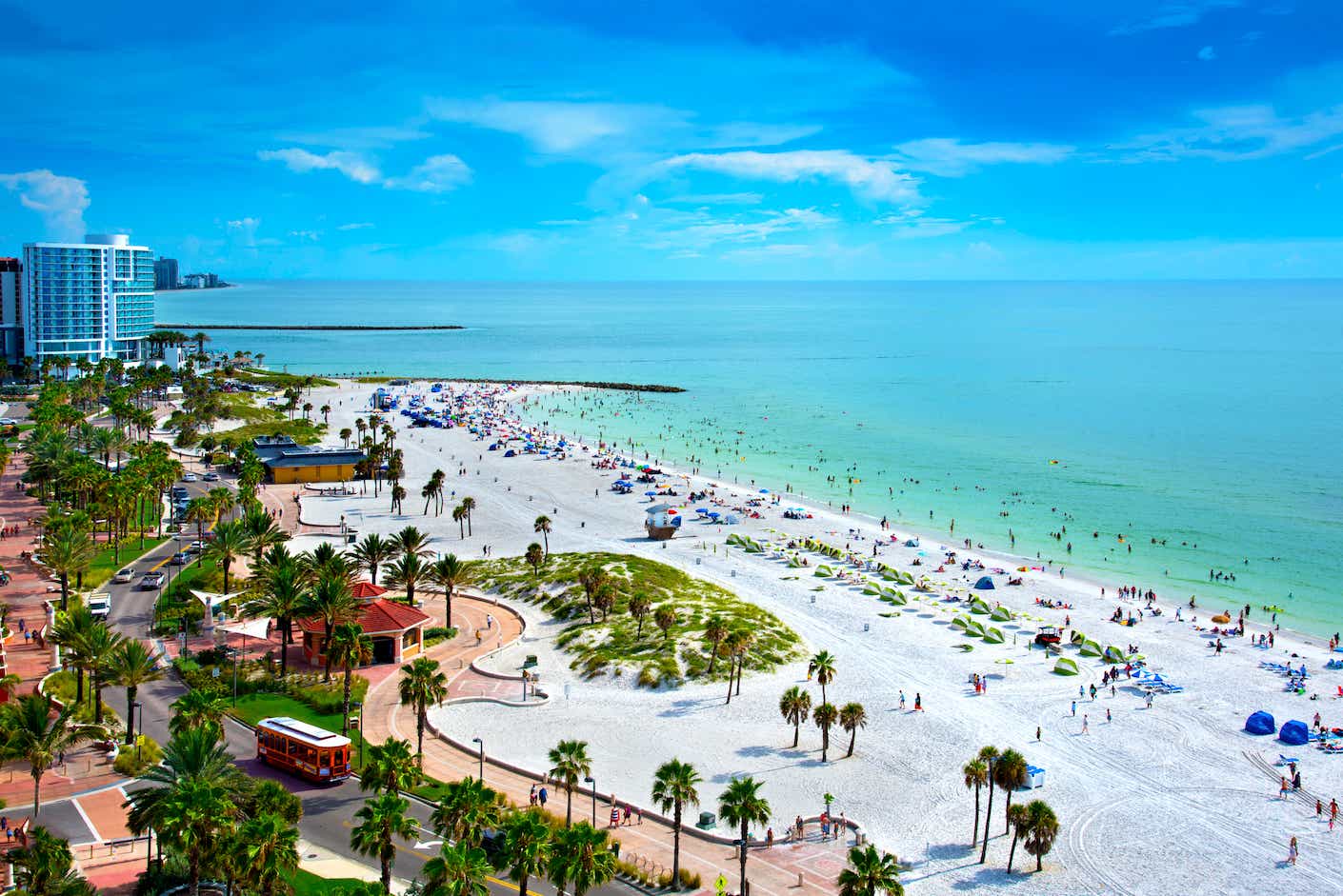 Sunny Clearwater beach with white sand, blue water, and a bustling downtown scene including high rises and palm trees.