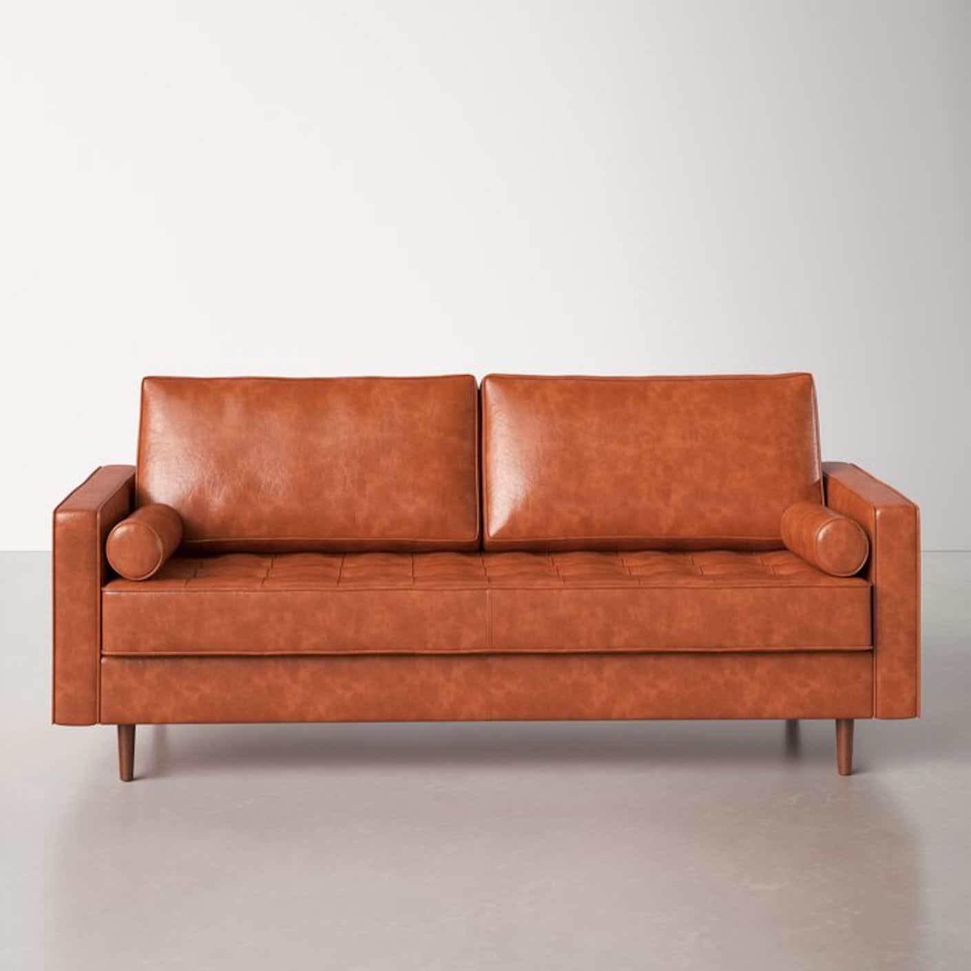 A caramel-colored, mid-century modern leather couch is pictured in a stark room.
