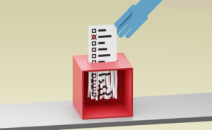 a hand putting a ballot into a box, where it's being shredded