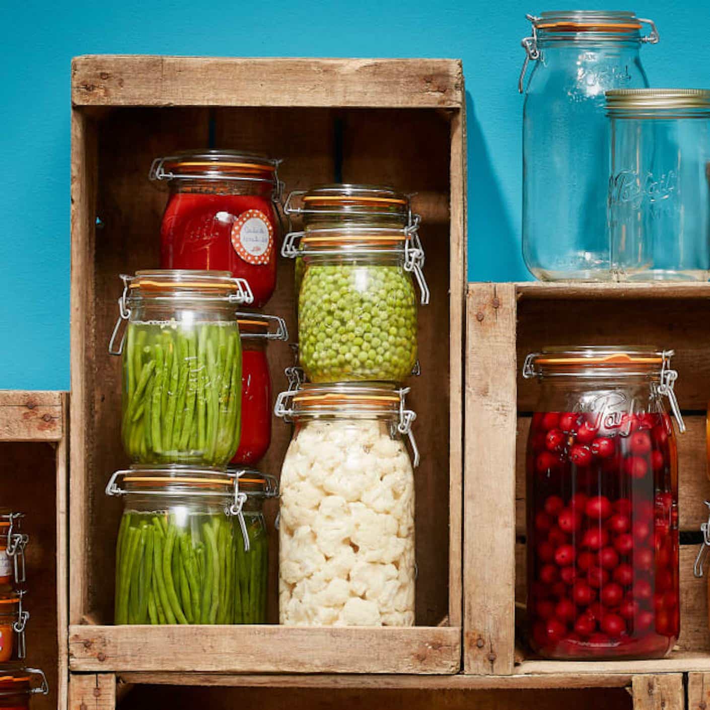 Stacks of clear, glass food storage containers full of food sit stacked on a brown wooden shelf.