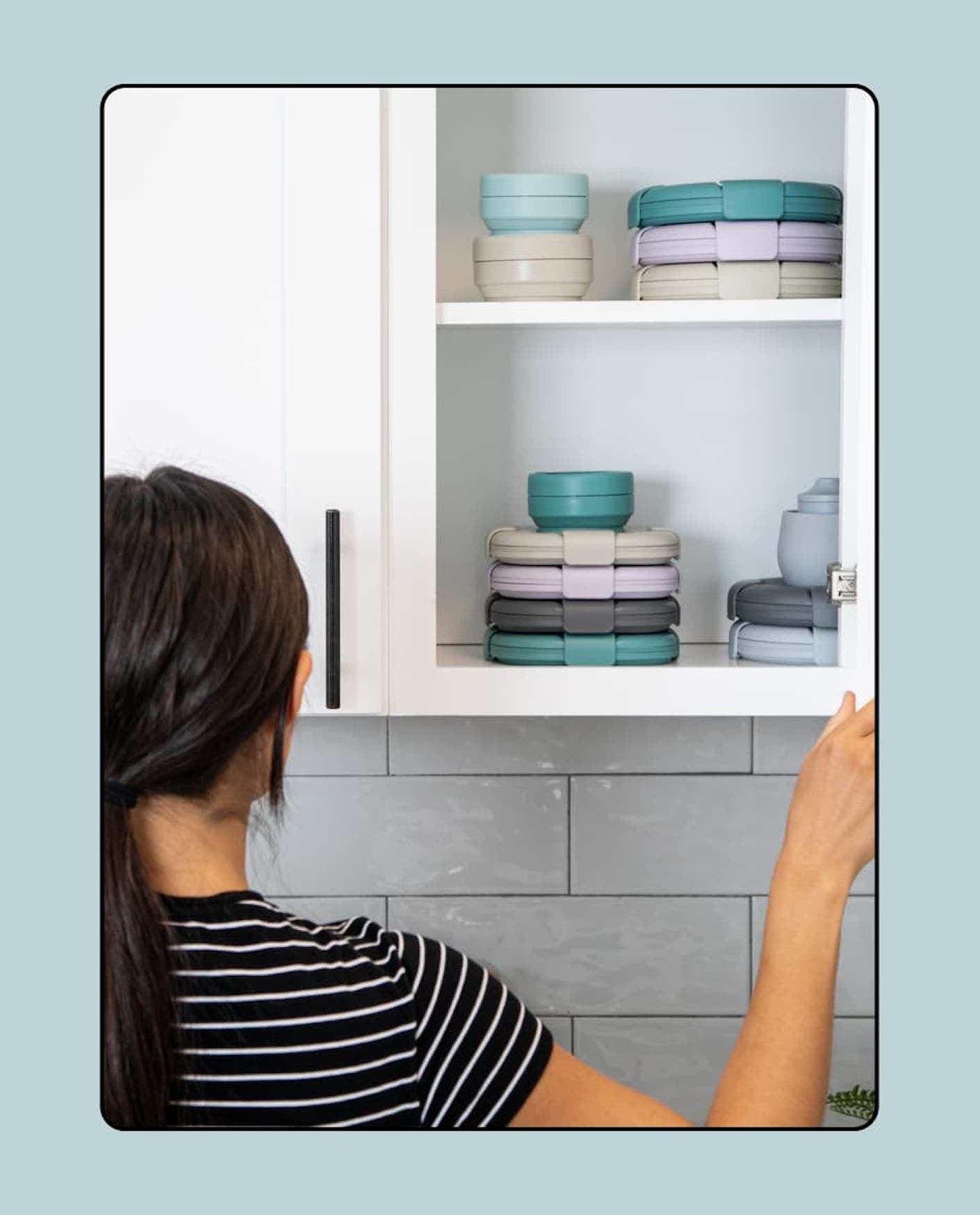 A woman opens a white cabinet full of blue food storage containers.