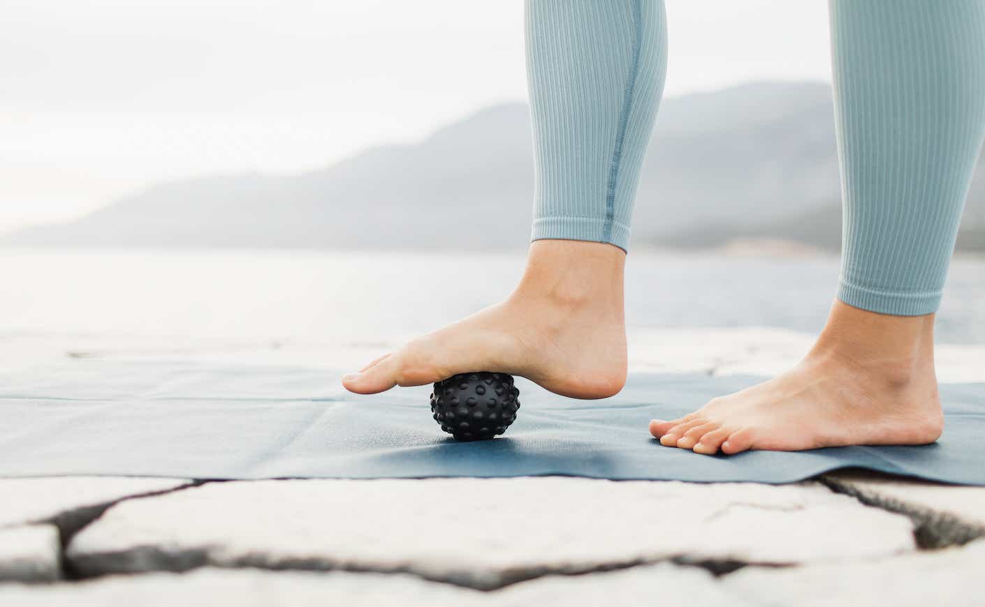 A close up of someone's lower legs and feet as they do footwork with a small black ball with a foggy beach in the backgound.