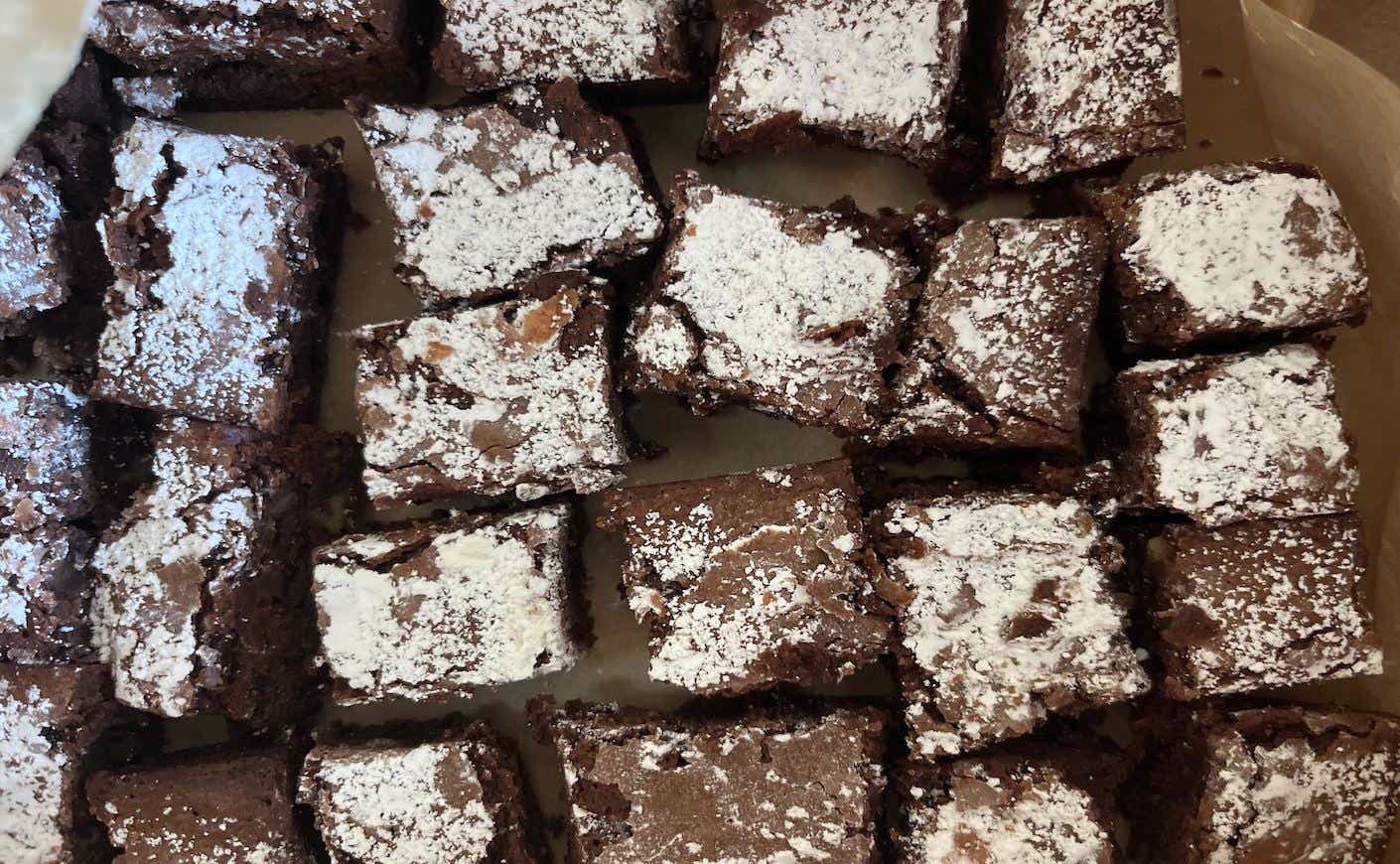 A tray of cooked brownies sprinkled with confectioner's sugar.