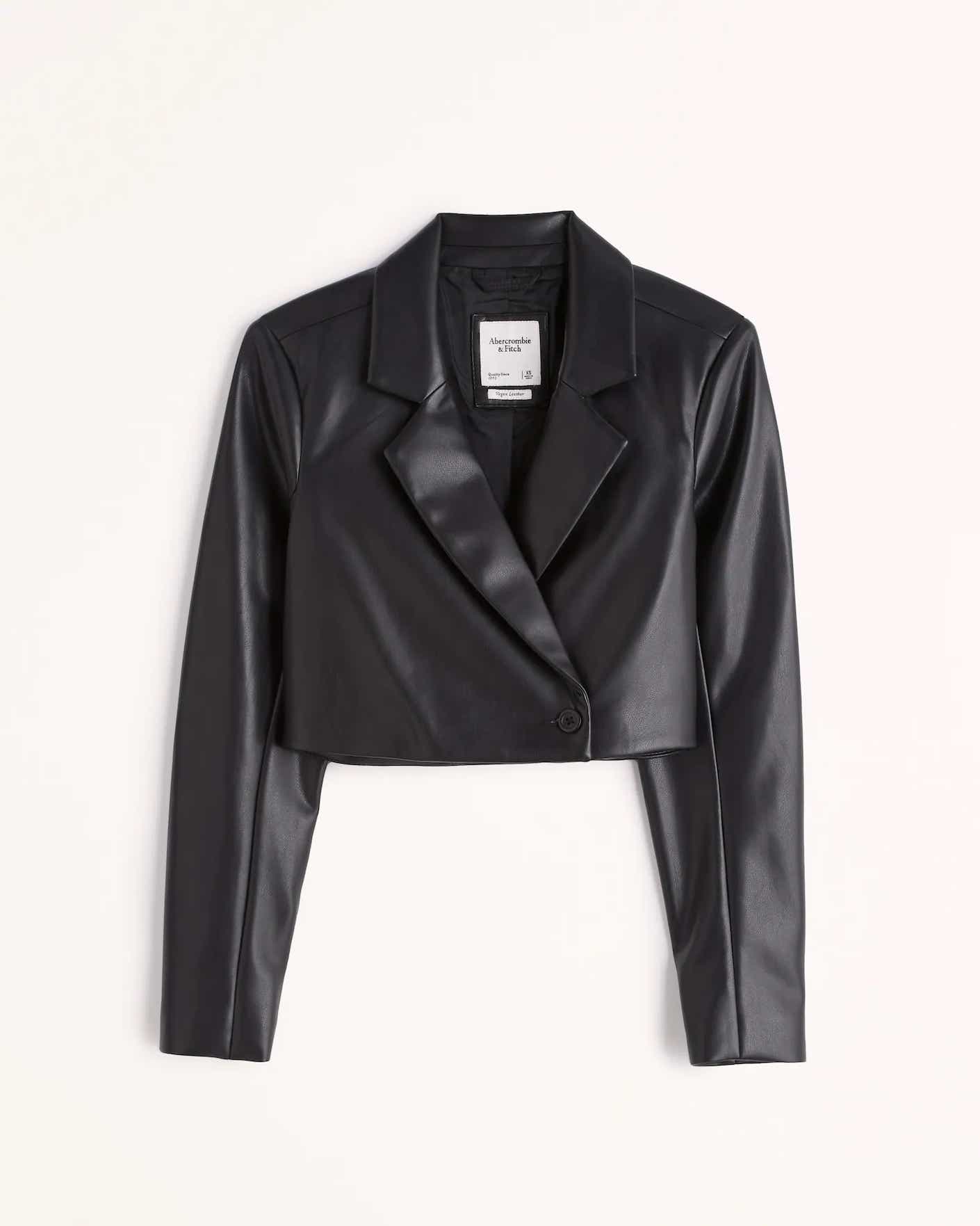 A cropped black leather blazer with a single button at its center lies flat on a white surface.
