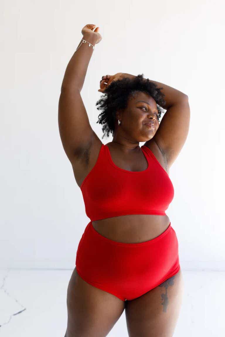 A woman poses in a bright red pair of high-waisted underwear and matching bra.