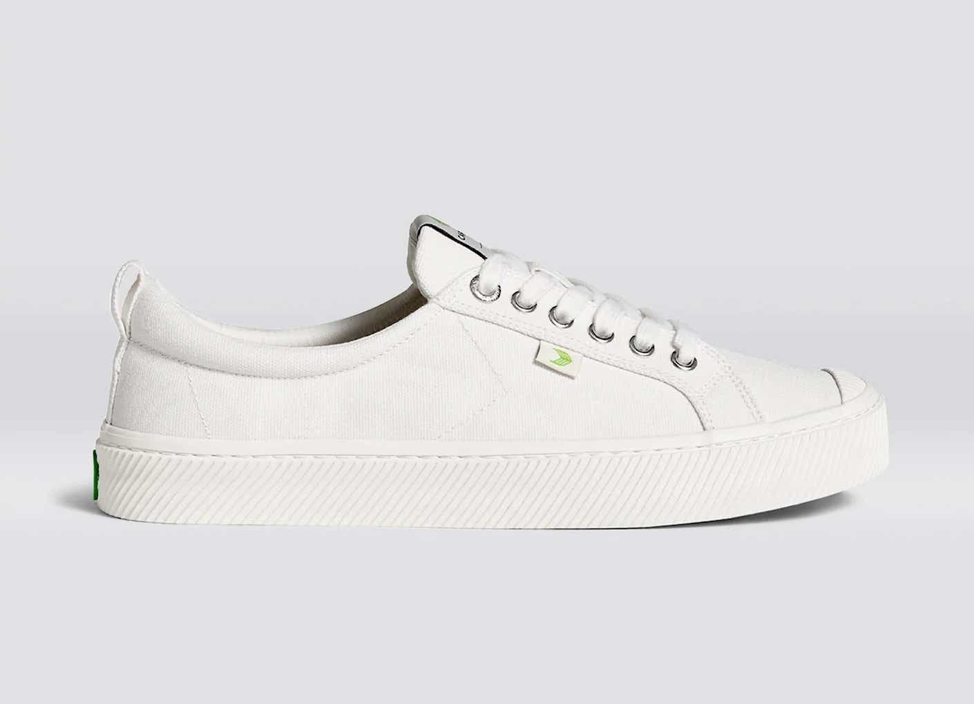 A pair of stark, white, low-top sneakers pictured in front of a white background.