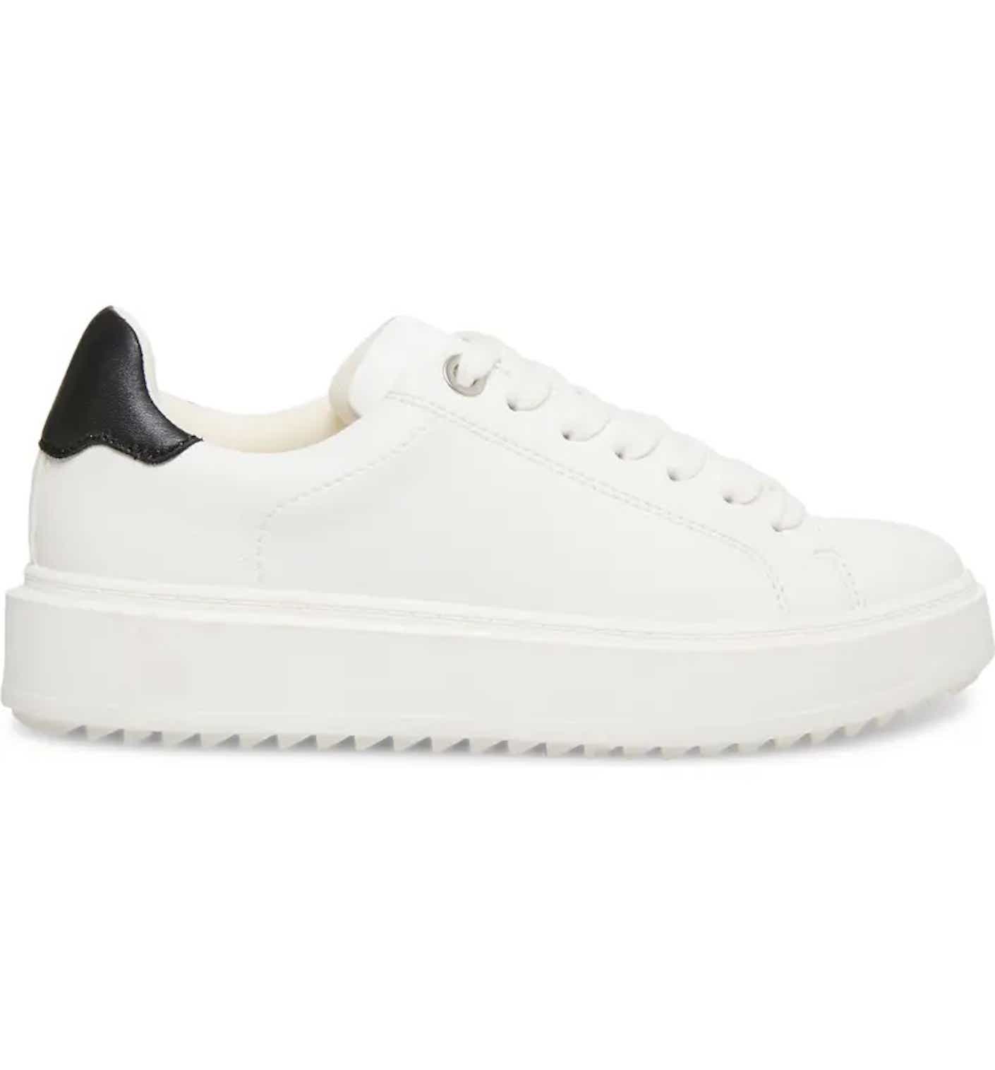 A minimalistic white platform sneaker with a black leather back pictured in front of a white background.