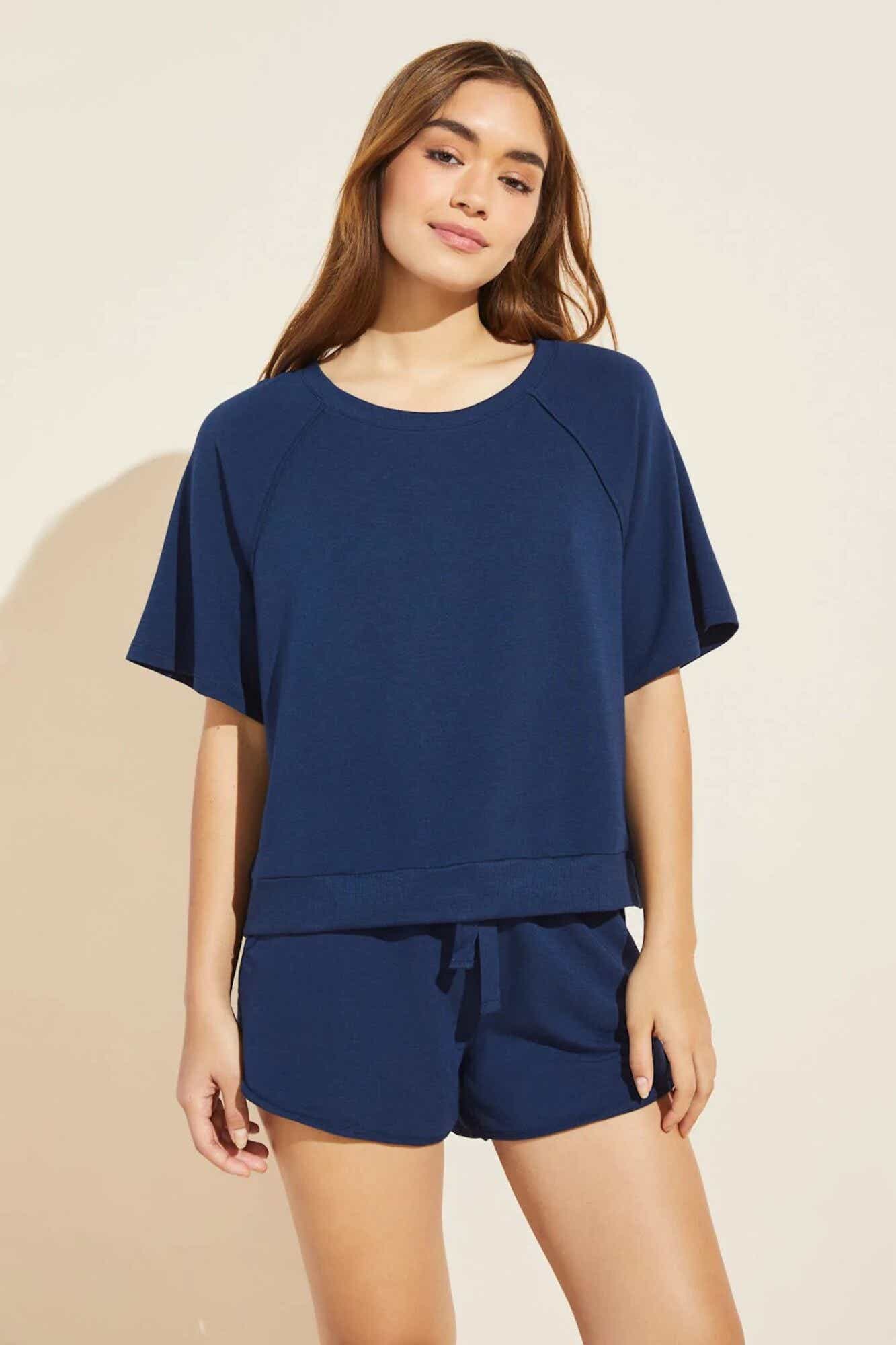 A smiling woman wears a loose fitting, short-sleeved soft knit top paired with matching dark blue soft shorts.