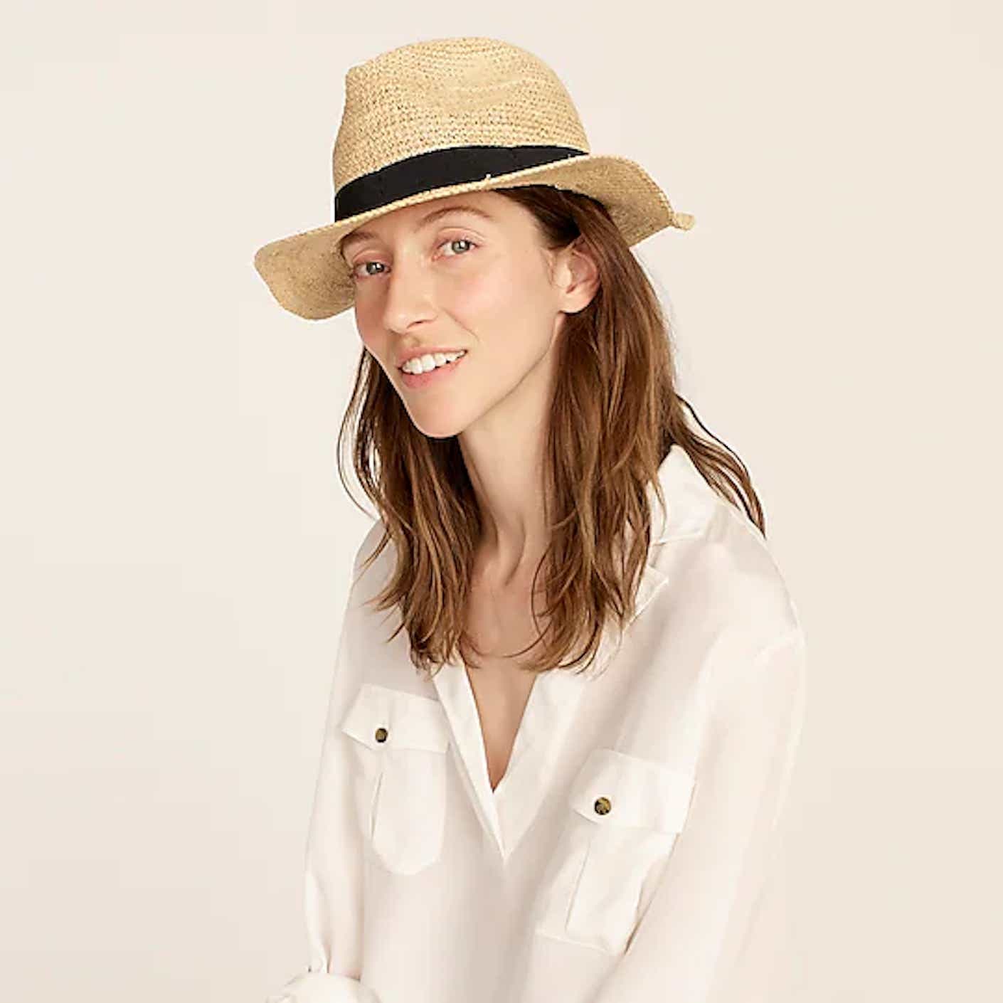 A woman wears a light, straw floppy hat with a medium brim and black band.