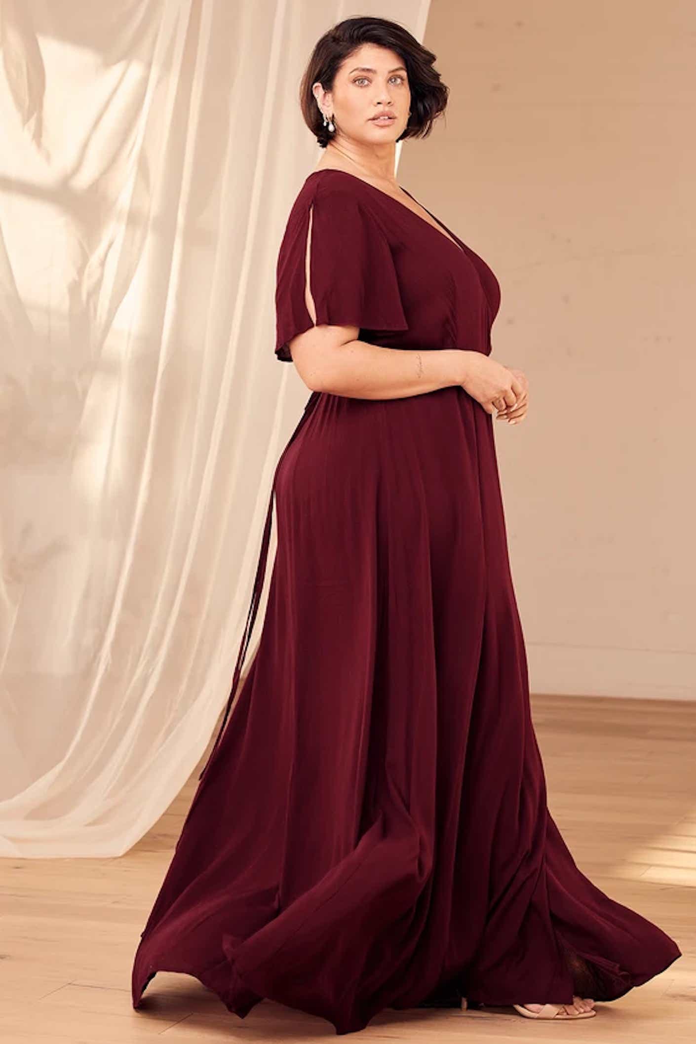 A woman wears a burgundy, floor length, wrap maxi dress that drapes dramatically.