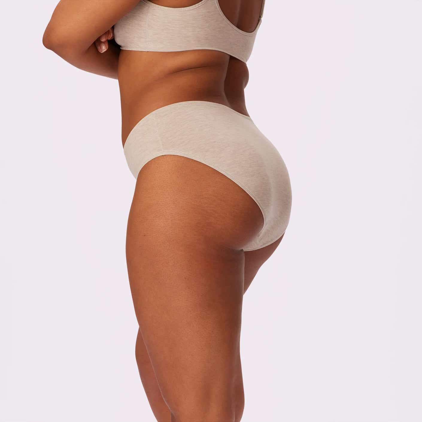 A woman with her arms crossed poses in a pair of beige underwear.