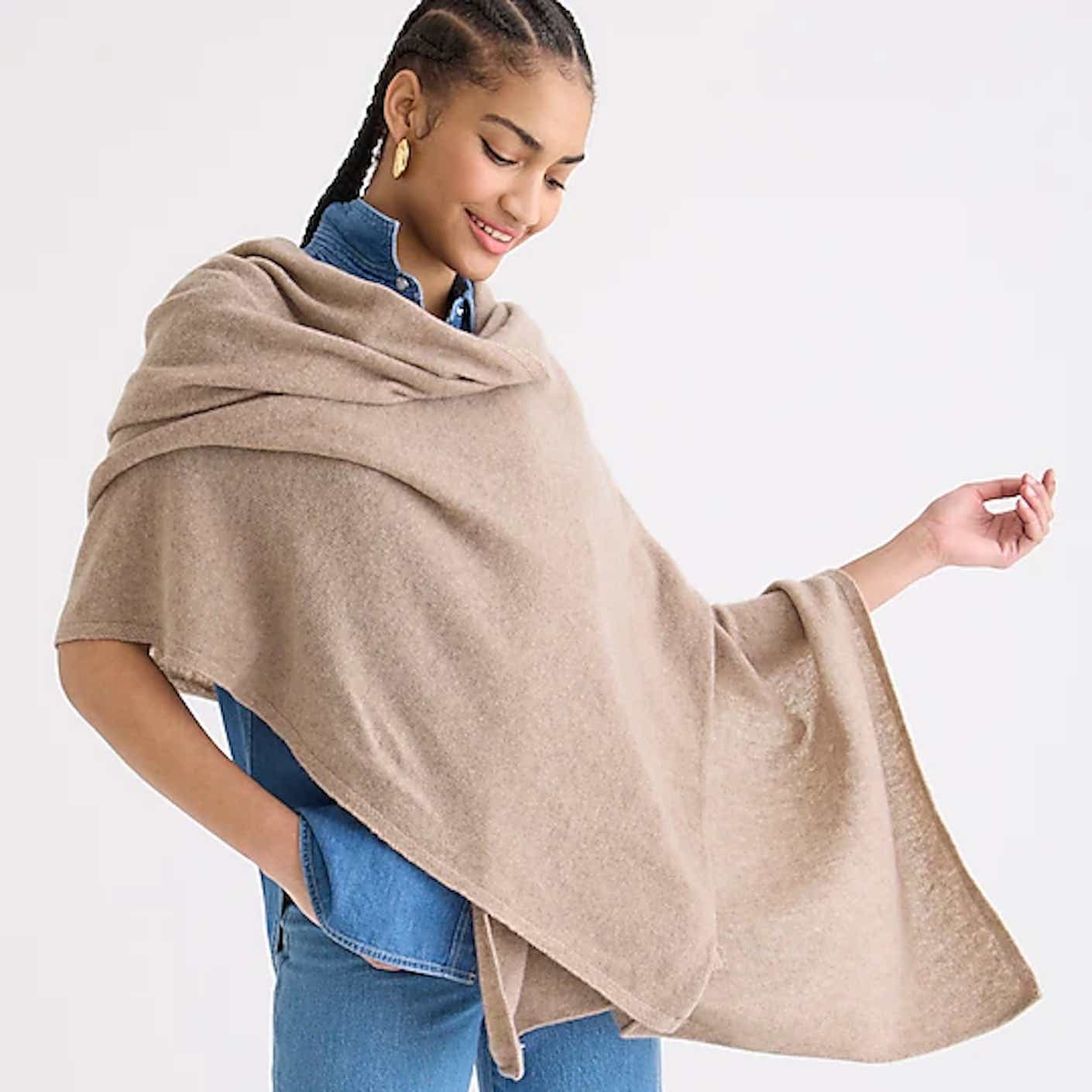 A woman wears a camel colored cashmere poncho that drapes over her shoulder.