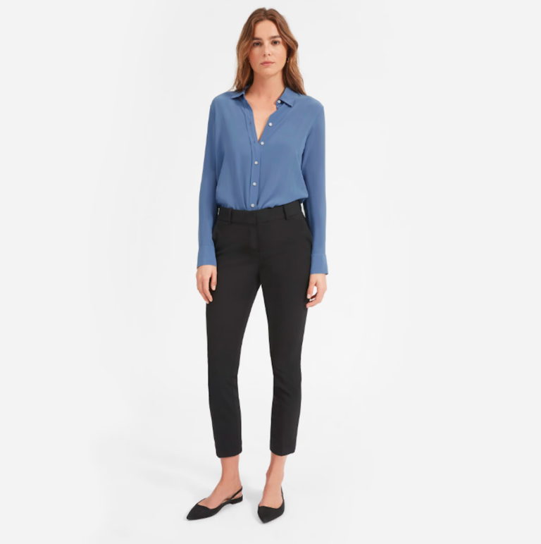 A woman wears a button down, blue, silk collared shirt with black jeans.