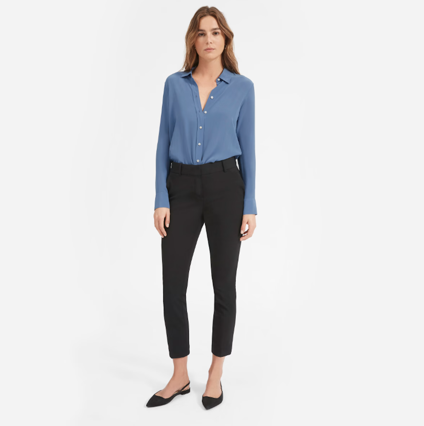 A woman wears a blue silk button down shirt with black jeans.