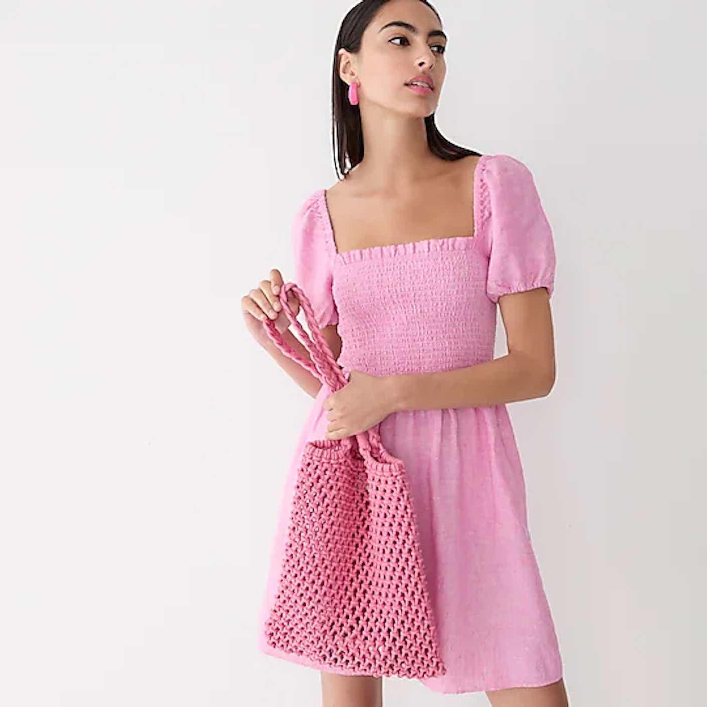 A woman wears a lightweight, soft pink mini dress with a smocked bodice and short, puffed sleeves.
