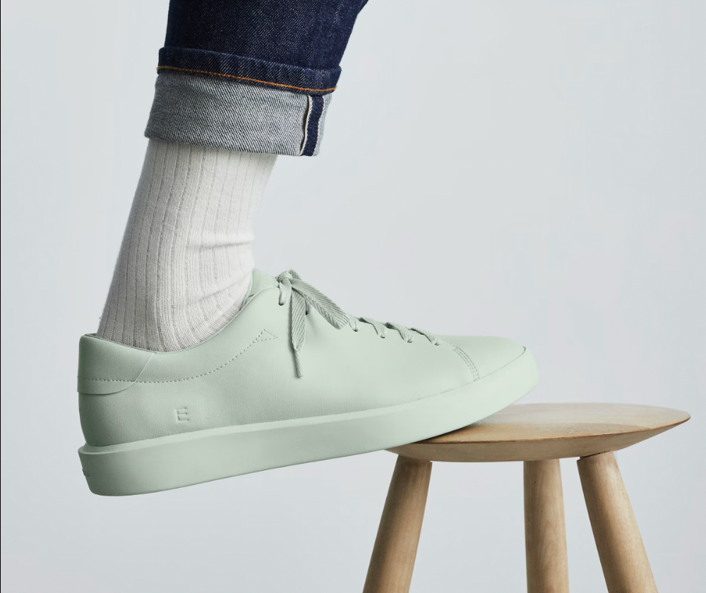 An image of a foot in a pastel green shoe balanced atop a wooden stool.