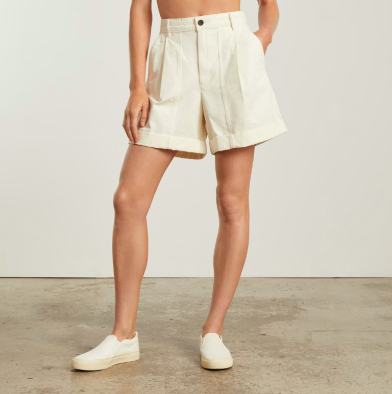 a person poses in structured, cream mid length shorts.