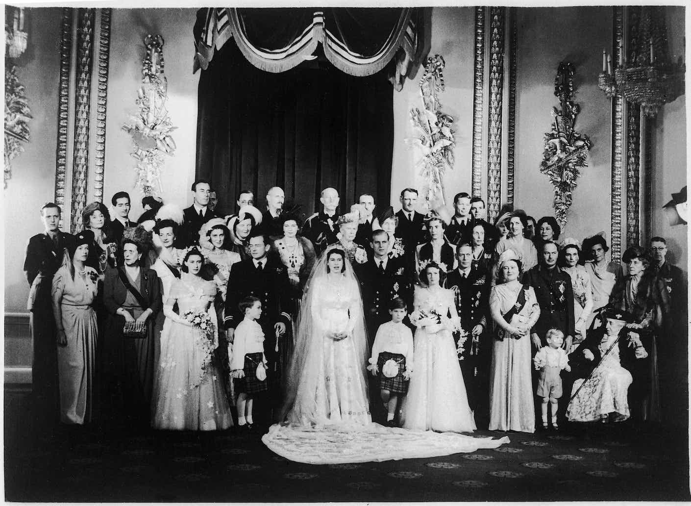 Wedding of Elizabeth II and Lt. Philip Mountbatten: the queen stands in a white dress in front of a large wedding party.