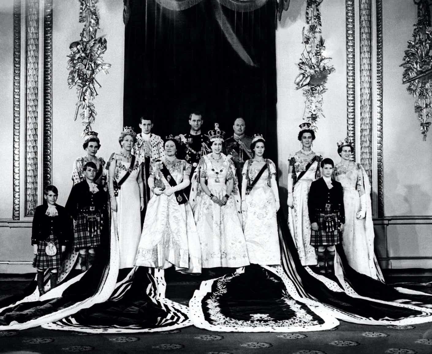 Queen Elizabeth II with her family on the Queen's Coronation's day at Buckingham Palace on June 2, 1953. She wears a long dress and crown.