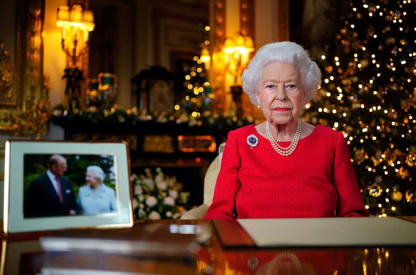Queen Elizabeth II records her annual Christmas broadcast in the White Drawing Room in Windsor Castle in 2021. A portrait of her and her husband sits in the foreground.