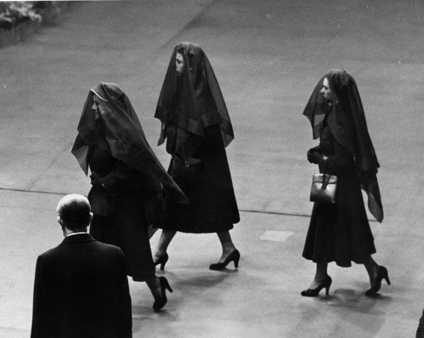 Left to right: Queen Elizabeth the Queen Mother, Queen Elizabeth II and Princess Margaret attend the arrival of the coffin of King George VI at Westminster Hall, London in 1952. ALl three are dressed in black dresses and veils.