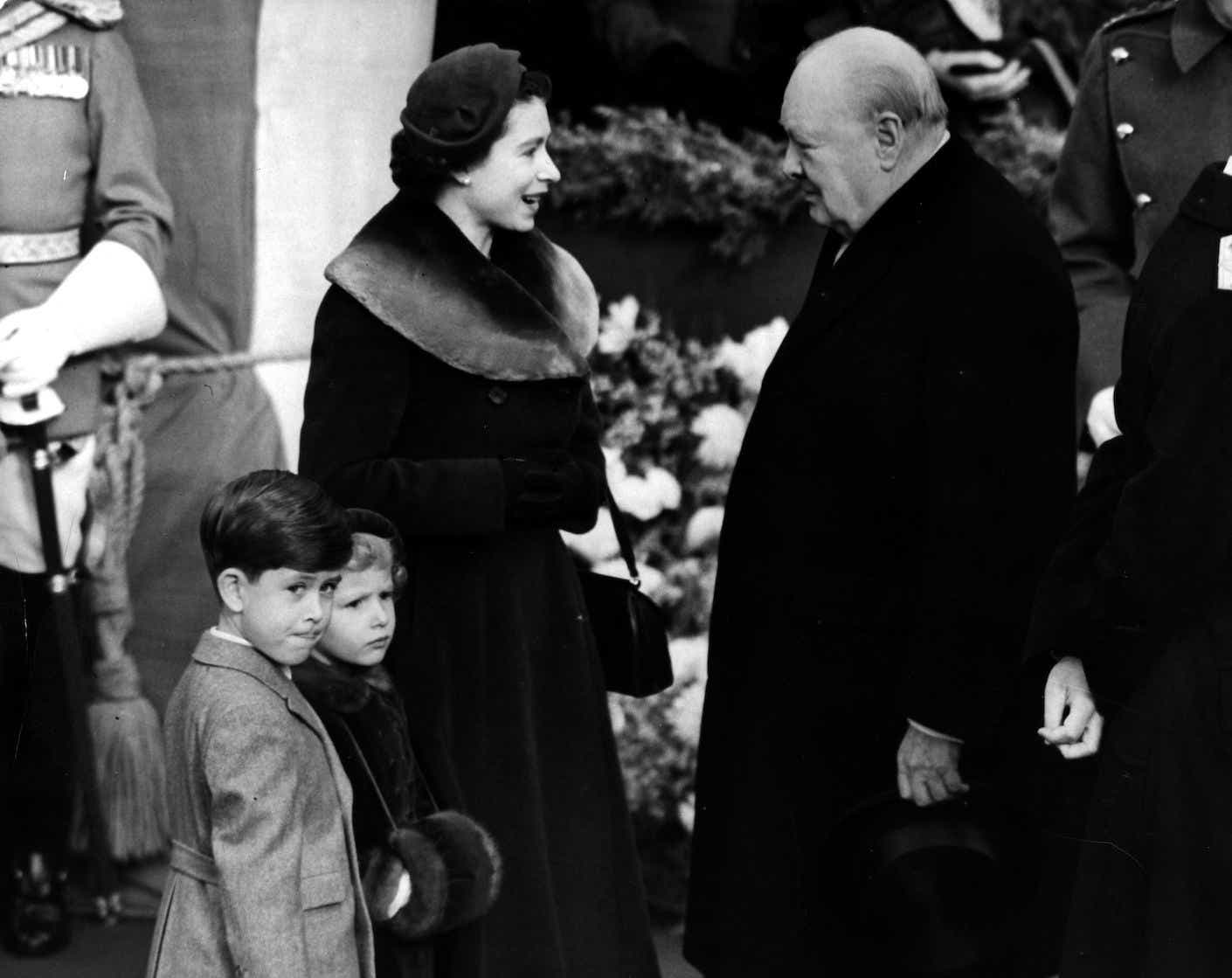 Queen Elizabeth II with Prince Charles and Princess Anne chat with Sir Winston Churchill in 1953 outside of a car.
