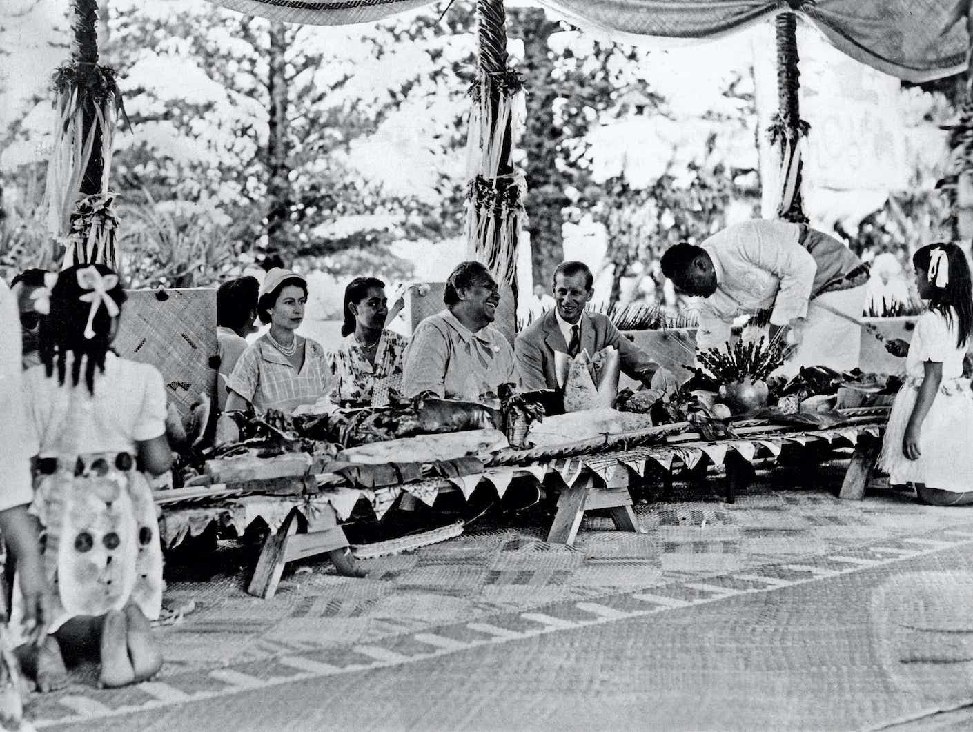 Queen Elizabeth II and Prince Philip with the Queen of Tonga at a feast at which a roasted pig was placed in front of every person, during the Royal Tour of the Commonwealth.