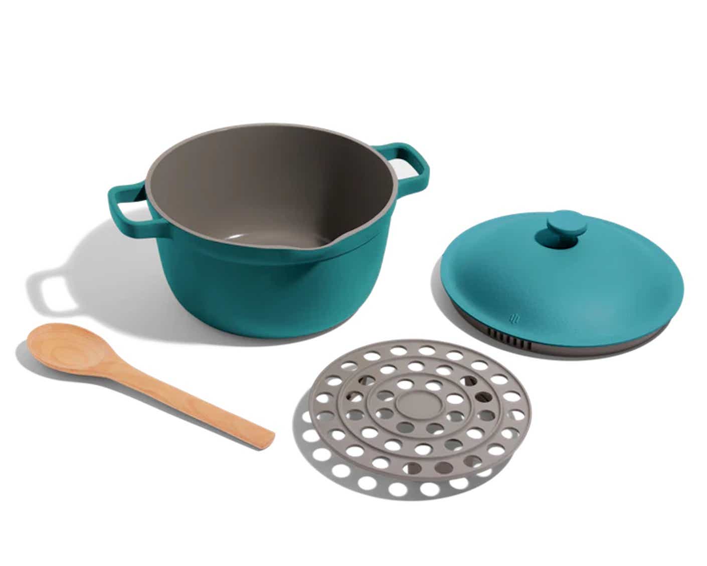 A ceramic Dutch oven, lid, wooden spoon, and metal colander sit together.