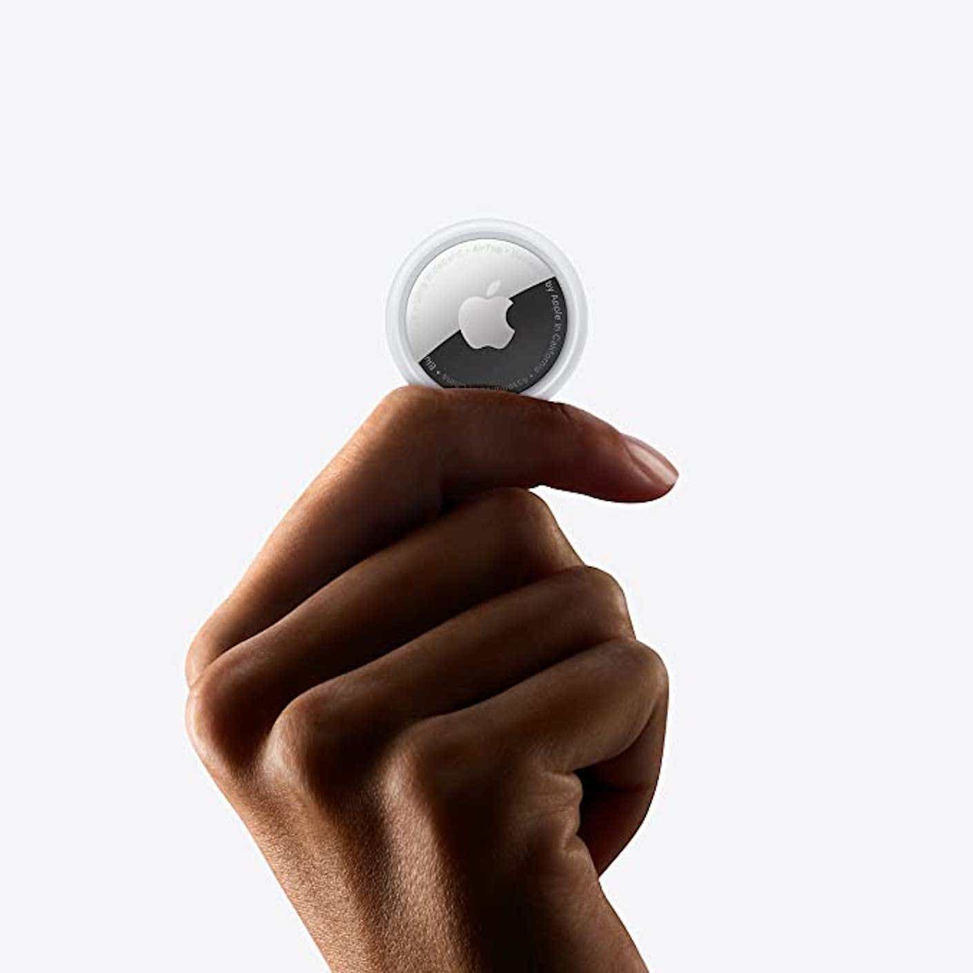 A disembodied hand holds up a single, circular, silver and white Apple AirTag.
